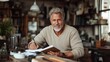 © familymedia - A mature man with a friendly smile writes in a notebook inside a rustic and cozy studio, surrounded by diverse objects and natural warm light filtering through windows.