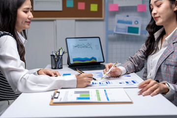 Two businesswomen analyzing charts and graphs on desk in office