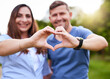 © peopleimages.com - Hands, heart and couple with smile, outdoor and sign for love in relationship, shape and portrait. Nature, man and .bonding with woman, happy and gesture for commitment in marriage or together in USA