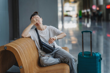 Young tired unhappy woman traveler waiting for flight or train departure with suitcase and at airport or train station, flight delay cancellation concept