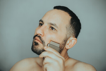 Young man shaving his beard off with an electric shaver