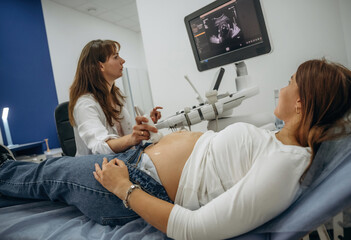 Monitor with graphical representation of scan. Pregnant woman undergoing ultrasound test