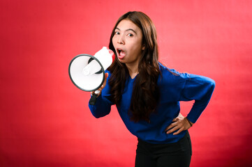 An Asian woman wearing a blue sweater is holding a red and white megaphone while speaking into it. She appears to be shouting or making an announcement. The background is solid red