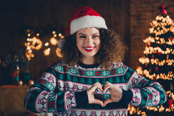 Portrait of nice young woman show heart symbol wear sweater new year xmas garland lights flat indoors