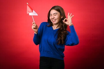 An Asian woman enthusiastically holds the Indonesian flag in her right hand while making an 