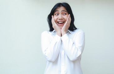 carefree asian young business woman shocked looking aside at empty space wearing white formal suit shirt, touching her face with two palms surprised, standing over isolated background