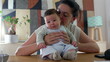 © Marco - Mother smiling warmly at her baby while holding the child on a table in a cozy indoor setting. peaceful family bonding moment between a mother and her happy baby