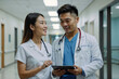 © polack - Two Asian doctors are standing in a hallway, one of them holding a tablet, they are smiling and seem to be discussing something important