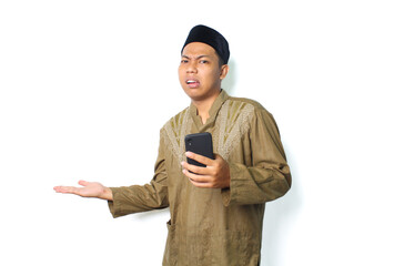 confused asian moslem man wearing islamic clothes presenting to beside with holding mobile phone isolated on white background