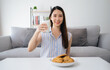 © Suriyawut - A woman is sitting on a couch with a glass of milk and a plate of cookies