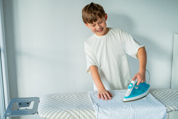 Cute 10 year old boy is doing homework and ironing clothes. Household appliances.