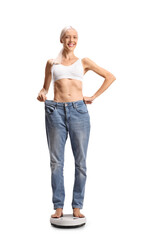 Wall Mural - Happy young woman standing on a weight scale in a big pair of jeans