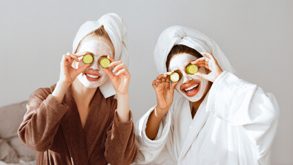 Happy multiracial girlfriends in bathrobes and face masks on covering eyes with avocado halves, face care concept, panorama