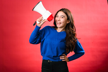 An Asian woman wearing a blue sweater is holding a red and white megaphone while speaking into it. She appears to be shouting or making an announcement. The background is solid red