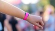 © cvetikmart - Close-up of a person's wrist wearing a pink breast cancer awareness wristband, with a blurred outdoor event in the background, natural light. Breast Cancer Awareness Month