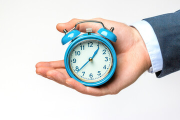 A businessman's hand holds a blue alarm clock on a white background. The concept of the flow of time, time to action.