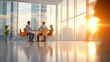 © Nano Photos - Three people are having a meeting in a bright, modern office with large windows, allowing the warm sunset light to stream in.