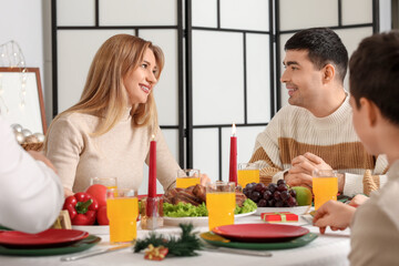 Happy young couple having Christmas dinner with their family at table in kitchen