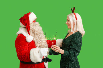 Santa Claus and beautiful mature woman in Christmas deer horns with sparklers on green background