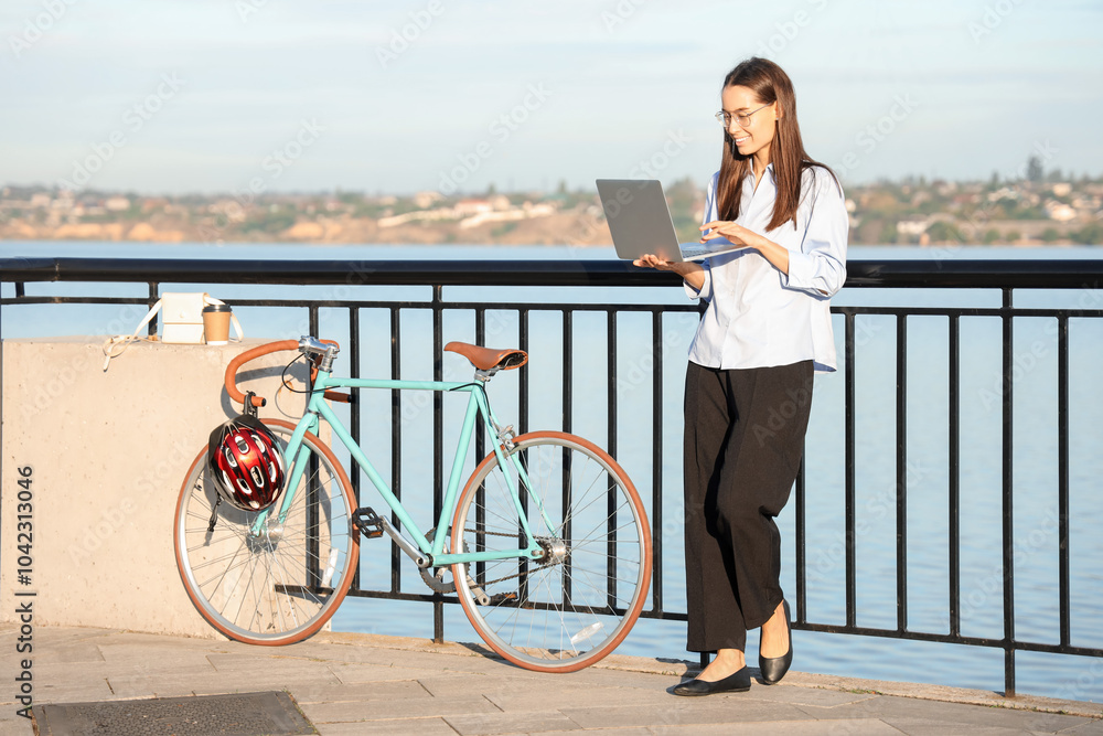 Young businesswoman with laptop and bicycle on bridge