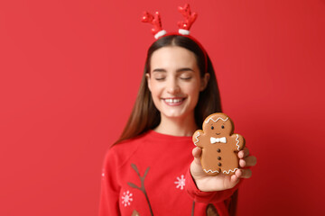 Poster - Young woman with tasty Christmas gingerbread cookie on red background