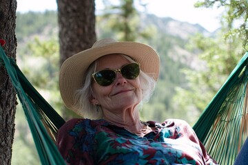 Elderly woman with white hair, wearing a sunhat and sunglasses, relaxing in a hammock between two trees in the mountains 1