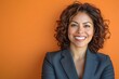 © Maelgoa - Middle-aged Latino woman with curly brown hair, wearing a business suit, smiling warmly on an orange background 1
