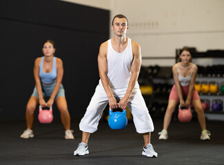 Sportive strong male in activewear swinging kettlebell during group exercise class in crossfit gym indoors