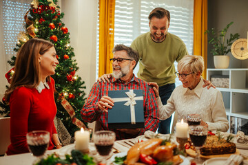 Wall Mural - Happy family giving christmas present to senior father during lunch