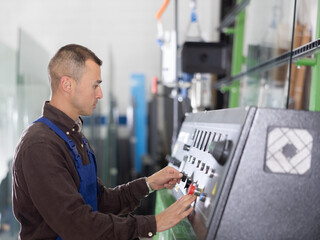 Confident glass factory worker at workplace with control panel, controlling technical process in workshop