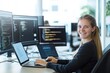 © Tondone - Young professional woman coding at multiple computer screens in modern office environment, smiling confidently at her workspace.