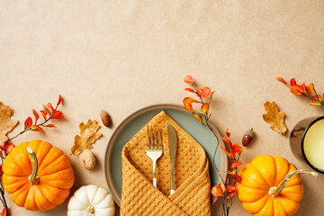 Autumn table setting with pumpkins, fall leaves, acorns, and a candle on a textured beige background. Thanksgiving, seasonal decor, cozy home setting