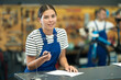 © JackF - Smiling attentive bicycle repairwoman in blue workwear filling out repair orders at counter, poised to expertly assist customers with bike maintenance in workshop..