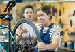 © JackF - Professional confident young female bicycle technician adjusting bike gear system, fixing sprockets on rear wheel using cassette pliers and explaining repair details to female client in workshop