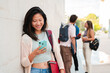 © Jose Calsina - Young chinese girl smiling while looking at her cellphone, leaning against a wall outside. Casual moment of a student or teenager using mobile technology to text, browse, or connect with friends
