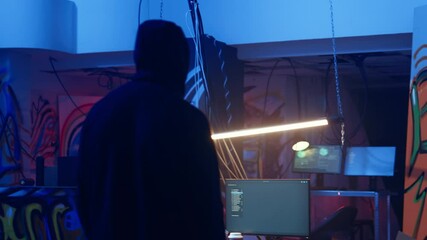 Hooded hacker arriving in hidden underground shelter, prepared to launch DDoS attack on websites. Cybercriminal starting work on script that can crash businesses servers, camera A