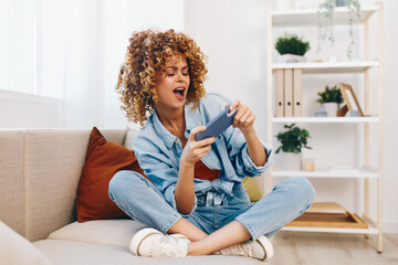 Joyful Woman Relaxing on Sofa, Holding Mobile Phone and Smiling at Home