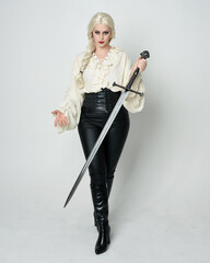 Sticker - Full length portrait of beautiful female model wearing vintage gothic fantasy blouse, leather pants, boots and blonde plaited hair, larp costume.  standing pose housing sword weapon in fighting action