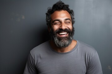 Wall Mural - Portrait of a handsome bearded Indian man laughing against a grey background