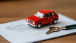 © Marketplace - Red toy car placed on documents with keys and pen, representing vehicle ownership and vehicle purchase agreements.