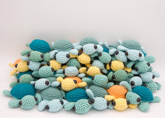 Pile of many handmade crochet turtles in green and turquoise, yellow and orange on an off white background.