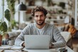 © ASGraphicsB24 - smiling young man using laptop while sitting at table in living room.