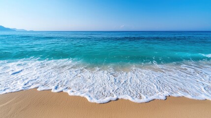 Wall Mural - A serene beach scene featuring clear blue water lapping gently against golden sand under a bright, cloudless sky.