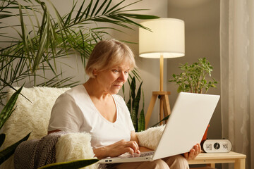 calm older mature freelance woman working at home using laptop typing on computer keyboard shopping 