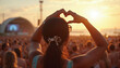 © Pawsitive Vibes - Female concertgoer creates a heart shape with her hands at a lively beachside music festival, with a diverse audience in the background, enjoying the sunset that reflects off the ocean