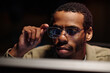 © DragonImages - Man sitting at a workstation adjusting his glasses while focusing intently on a task, showing concentration in a low-light environment