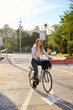 © Cavan Images - Young woman cycling joyfully on a paved path in an urban city
