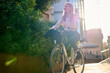 © Cavan Images - Business young woman biking through a sunlit urban area