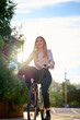 © Cavan Images - Business young woman biking through a sunlit urban area