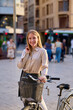 © Cavan Images - A smiling woman with a bicycle enjoys a sunny day in a bustling city